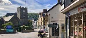 Lynton with church and clocktower, old car in foreground of pretty street with shops