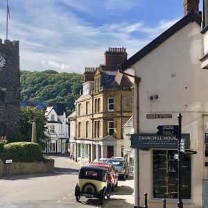 Lynton with church and clocktower, old car in foreground of pretty street with shops