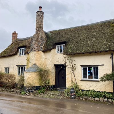 A yellow painted stone house with thatched roof on a grey and wet day in Bossington still sweet as ever