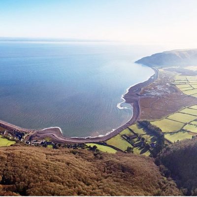 Photo from above of Porlock Bay and Bossington Beach looking up towards Hurlstone Point, with patchwork fields and heather in the foreground