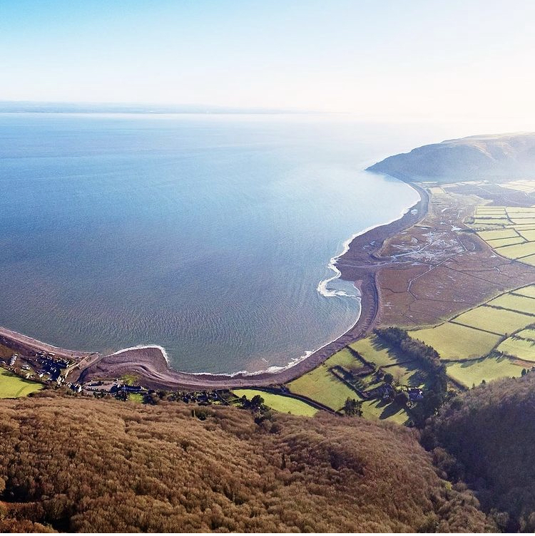 Photo from above of Porlock Bay and Bossington Beach looking up towards Hurlstone Point, with patchwork fields and heather in the foreground