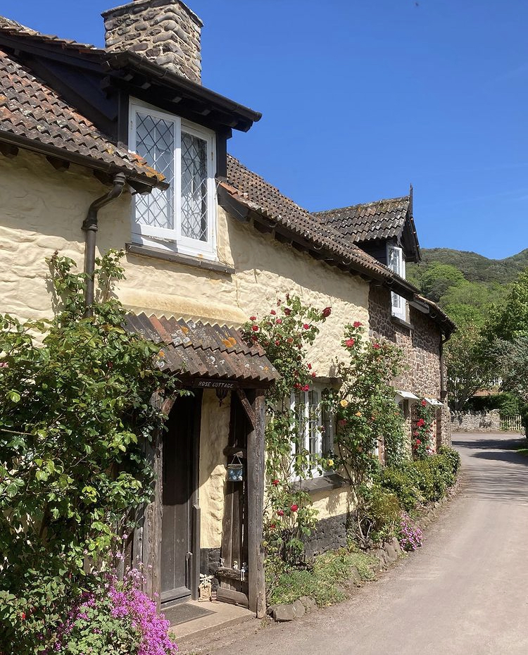 A cute house in Bossington with pretty plants and flowers growing up the yellow walls and a blue sky background