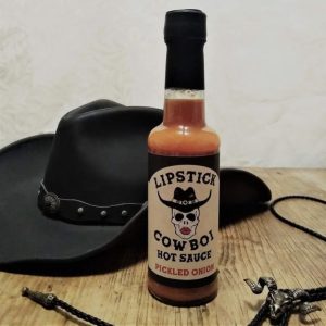 Hot sauce at the Lynton Christmas Market - a bottle of Lipstick hotsauce with a skull in a cowboy hat on the label, and a black cowboy hat in the background and bolo with a rams skull as the clasp in the foreground