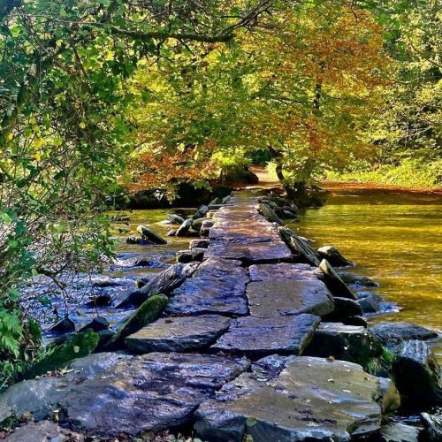 An inviting walkway - The Tarr Steps a clapper bridge made of stones across a river in Exmoor with greenery and dappled sunlight