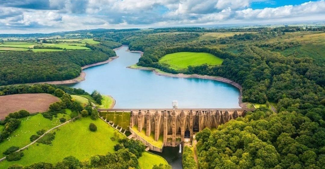 A beautiful photo of Wimbleball Lake and Reservoir on a sunny day with green fields surrounding, from above