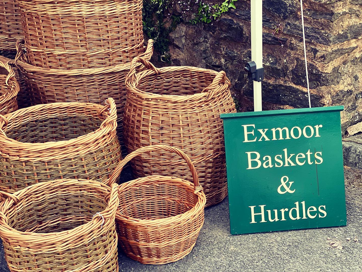 A selection of wicker baskets at a market stand and a green sign with white writing reading 'Exmoor baskets & Hurdles"