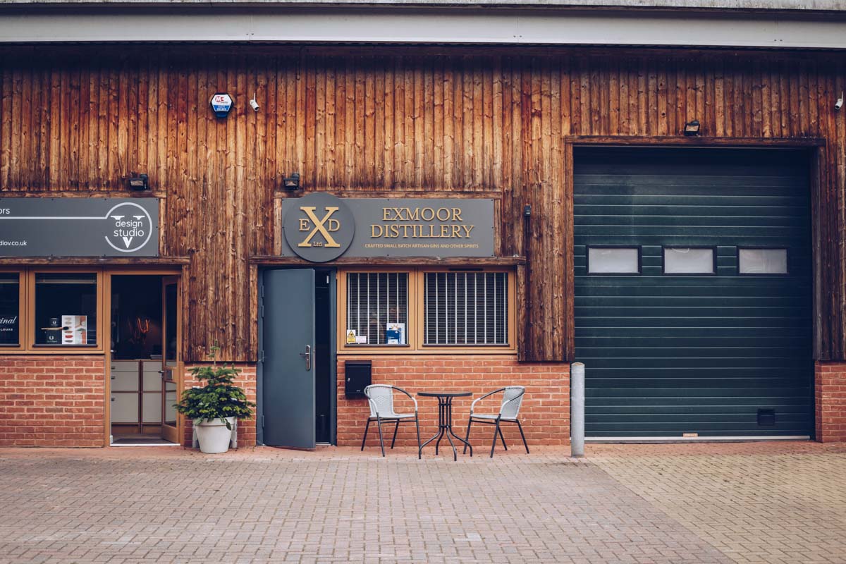 Exmoor Distillery - a building with beautiful wooden panelling and dark blue doors with a table set up outside the entrance and a sign above the doors