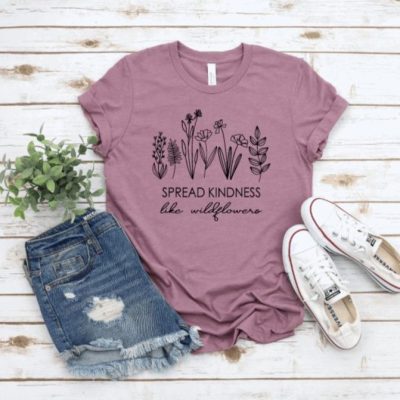 A pair of jeans shorts, a pair of converse trainers, a purple t shirt with wildflowers on it and a sprig of greenery on a whitewashed wooden background - Exmoor Summer Packing Essentials
