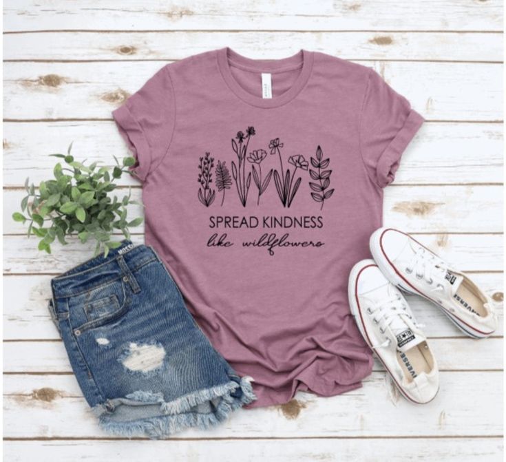 A pair of jeans shorts, a pair of converse trainers, a purple t shirt with wildflowers on it and a sprig of greenery on a whitewashed wooden background - Exmoor Summer Packing Essentials