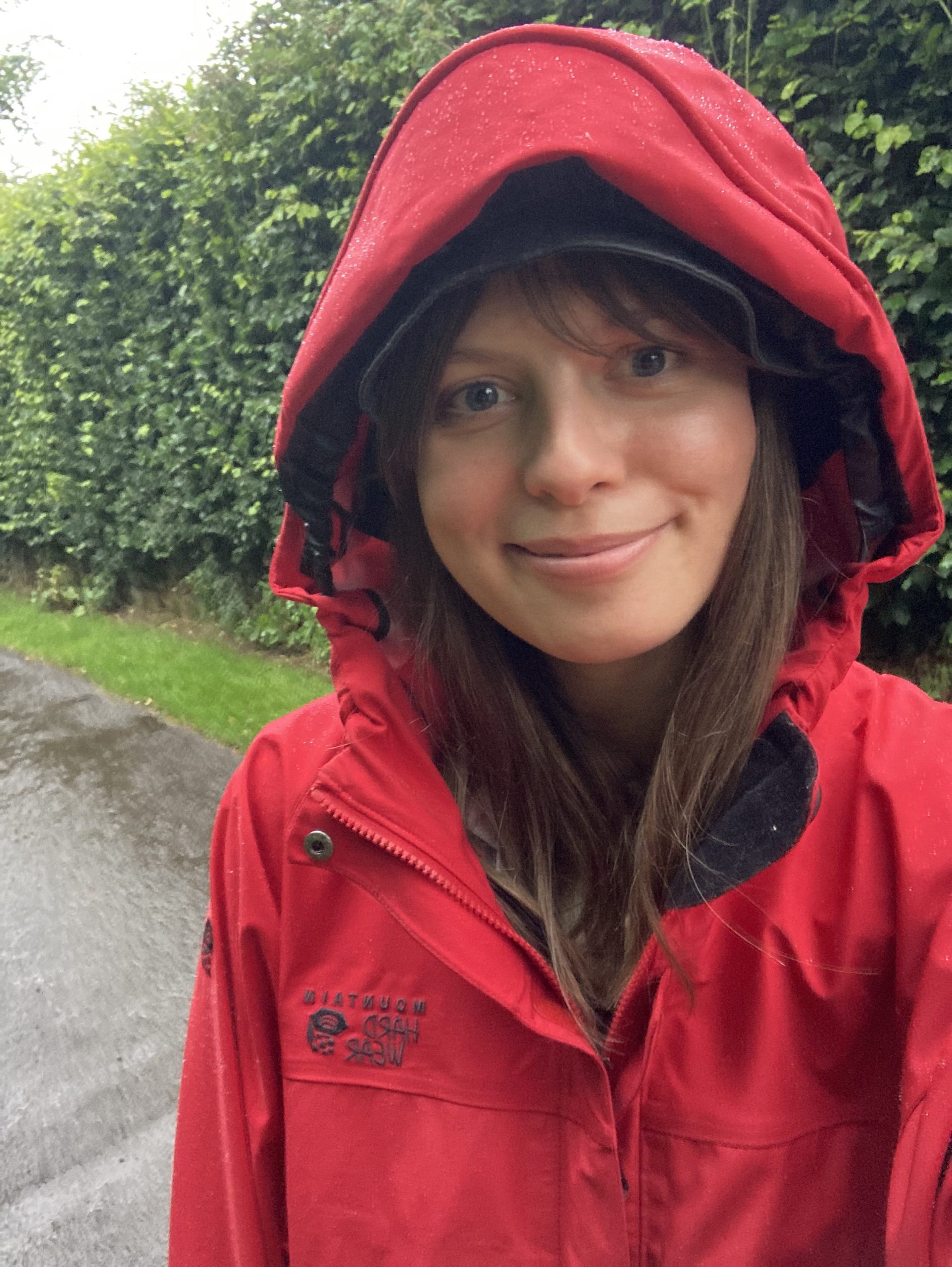 Smiling girl in raincoat with hood up in the rain in the countryside