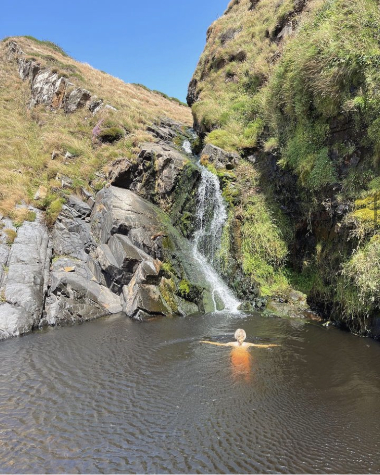 Girl wild swimming towards a waterfall along the South West Coast Path