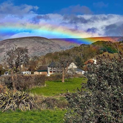 Rainbow over beautiful Exmoor countryside with a house in the distance nestled amongst trees below the impressive hills of the moors