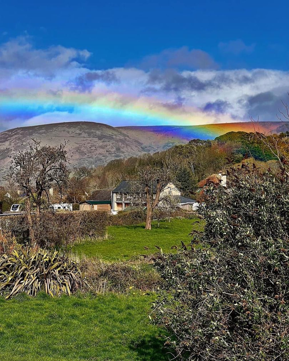 Rainbow over beautiful Exmoor countryside with a house in the distance nestled amongst trees below the impressive hills of the moors